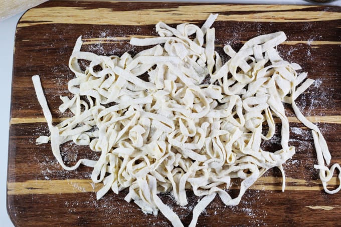A close up overhead shot of egg noodles on a cutting board.