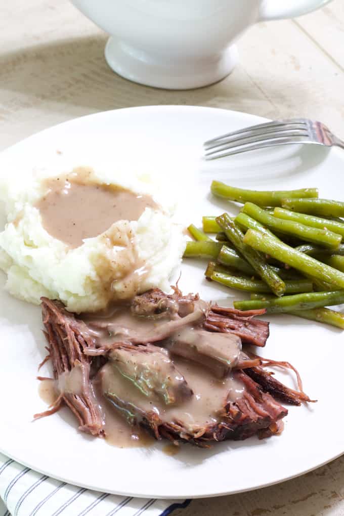 A plate with roast beef, mashed potatoes, gravy and green beans.