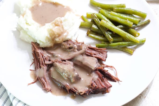 A white plate with roast beef and mashed potatoes smothered in gravy and green beans.e