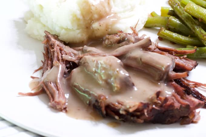 Very close up view of tender roast beef smothered in silky brown gravy.