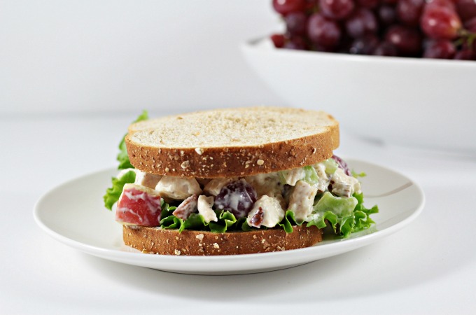 Front view of a chicken salad sandwich and bowl of grapes in the background.