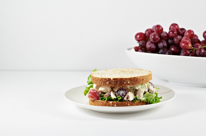 Front view of a chicken salad sandwich and bowl of grapes in the background.