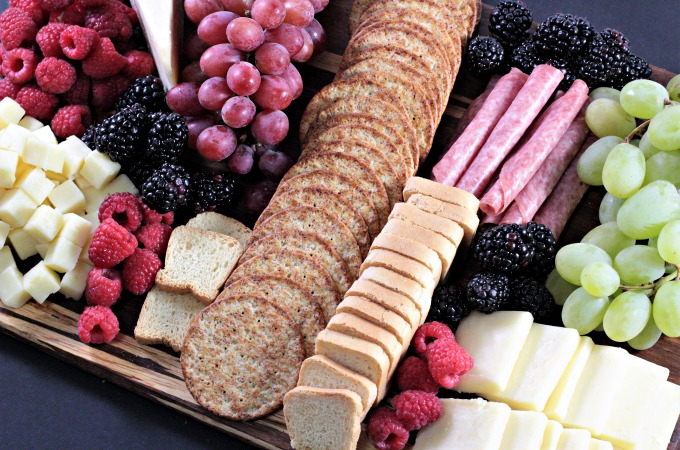 This Perfect Party Cheese Board features Stella Cheeses, Genoa Salami, crackers, mini toast, red and green grapes, raspberries and blackberries. 