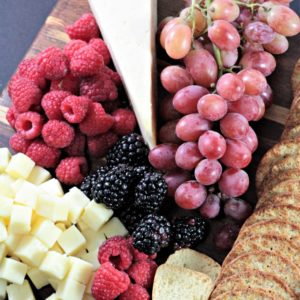 This Perfect Party Cheese Board features Stella Cheeses, Genoa Salami, crackers, mini toast, red and green grapes, raspberries and blackberries.