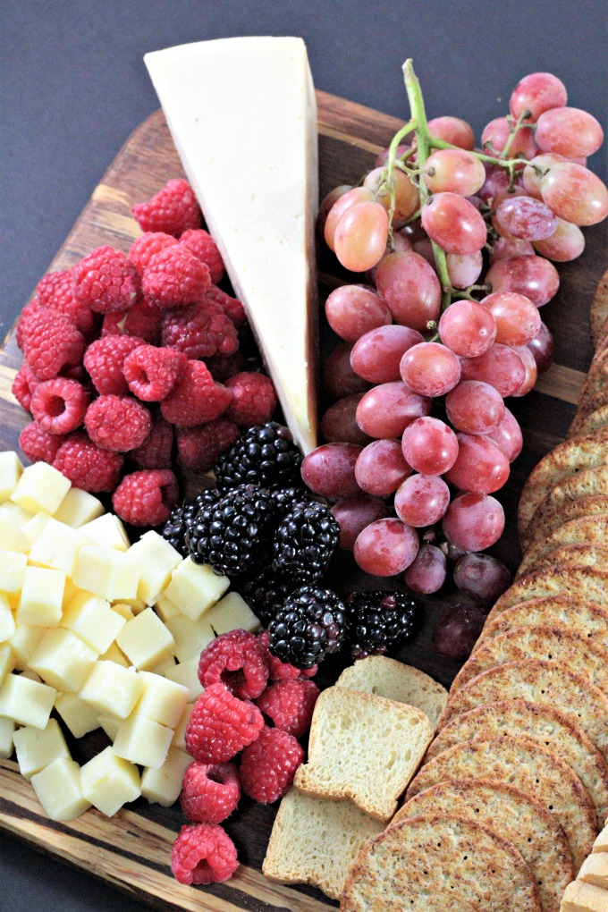 This Perfect Party Cheese Board features Stella Cheeses, Genoa Salami, crackers, mini toast, red and green grapes, raspberries and blackberries.