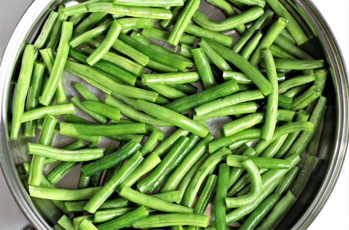 Raw green beans in a stainless steel skillet ready to be cooked.