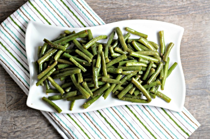 Green beans on a white plate sitting on a striped towel.