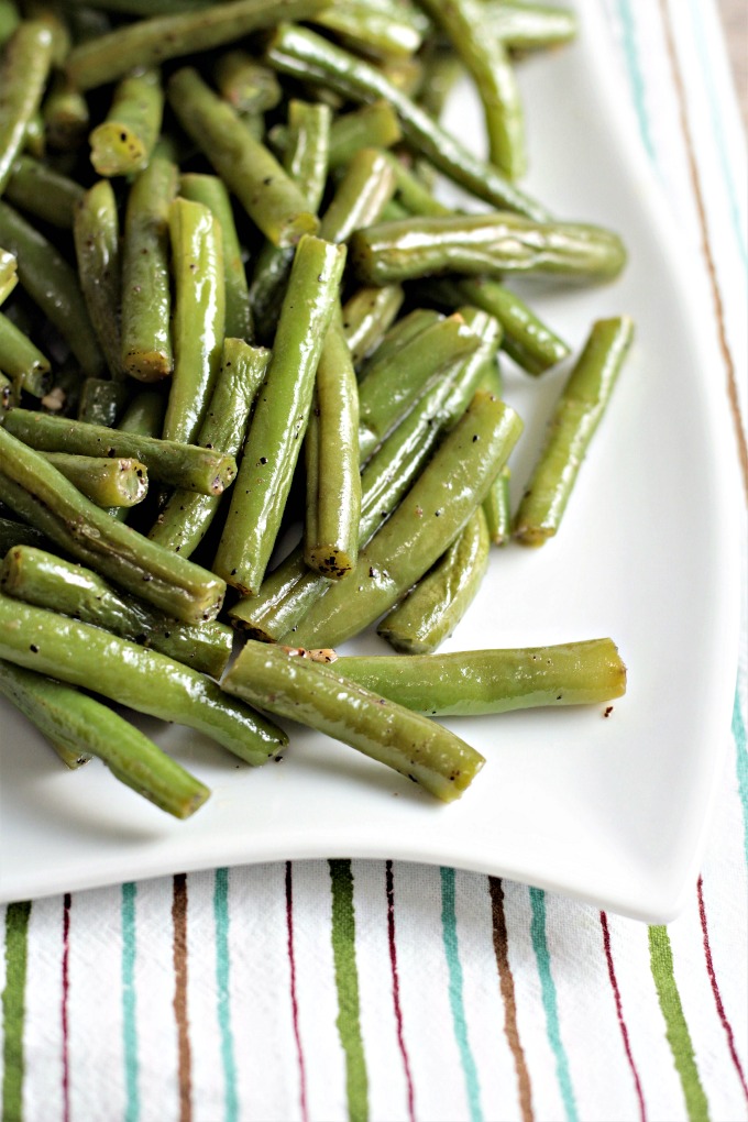 A side view of green beans on a white plate sitting on a striped towel. 