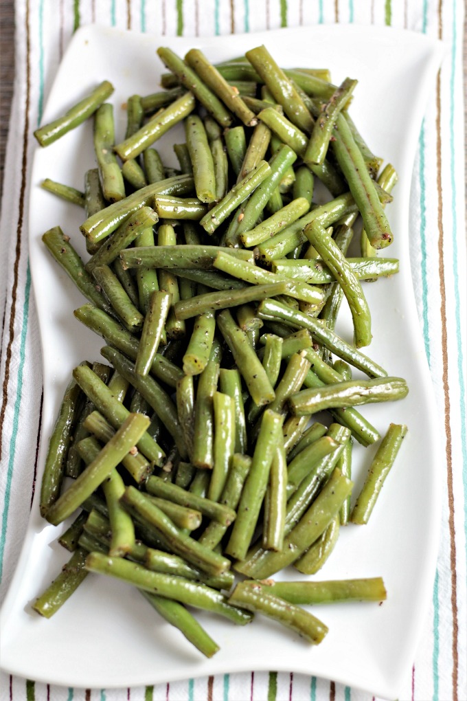 Angles shot of a white plate of green beans that is sitting on a striped tea towel. 