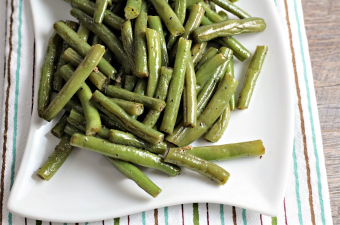 The bottom portion of a plate of green beans sitting on a striped towel.