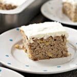 A close up side view of a piece of hummingbird cake topped with cream cheese frosting.