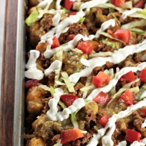 Loaded Beef Tater Tots (Totchos) feature nacho ingredients (ground beef, cheese, sour cream, salsa, and tomatoes) on tater tots instead of tortilla chips.