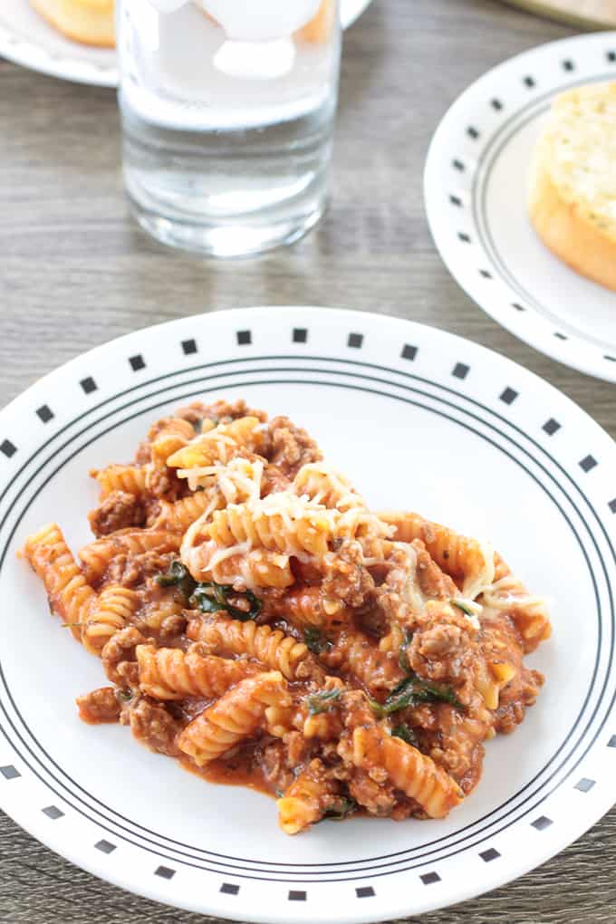 A plate of pasta, bread on a plate and a glass of water on a table. 