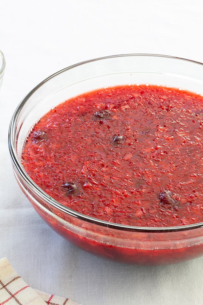 A large glass bowl full of cranberry raspberry jello salad on a white tablecloth.