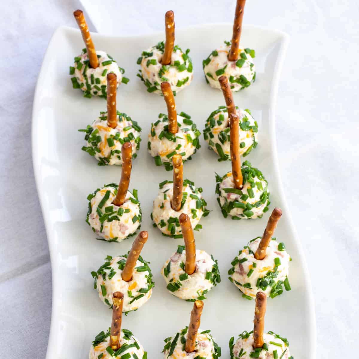 Close up overhead shot of fifteen mini salami cheese balls on a white plate.