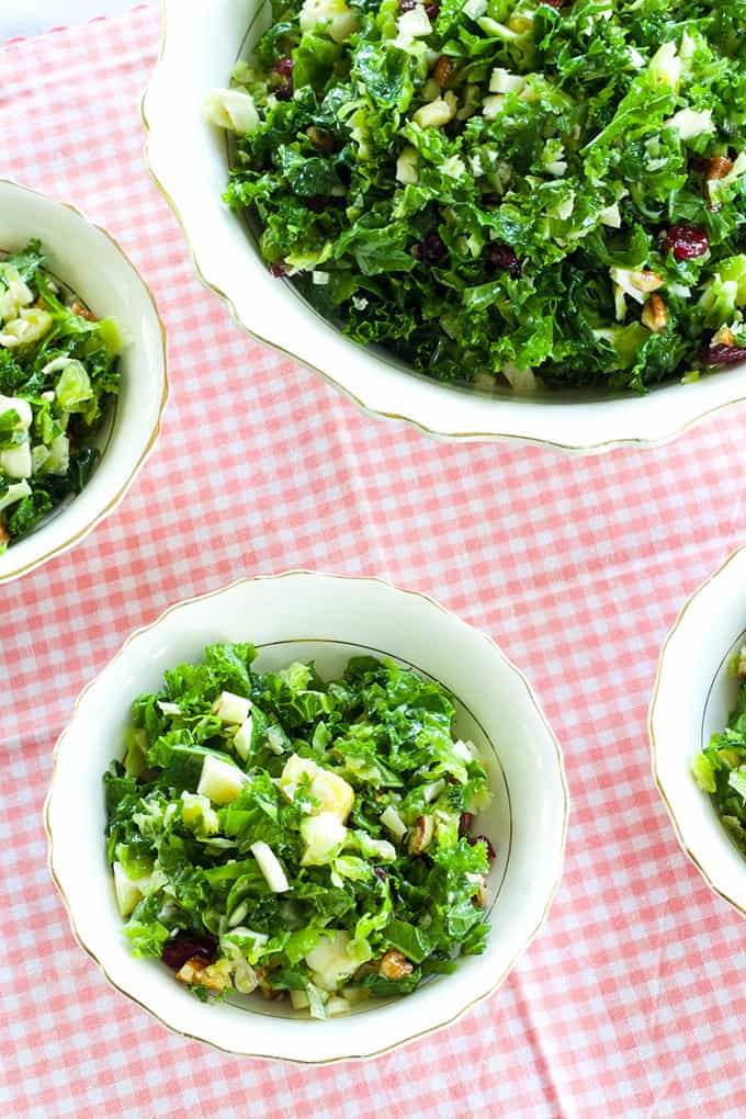 Close up view of one large and three small bowls of brussels sprouts and kale salad. 