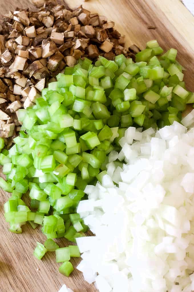 A plie of chopped mushrooms. celery and white onion all on a wooden cutting board. 