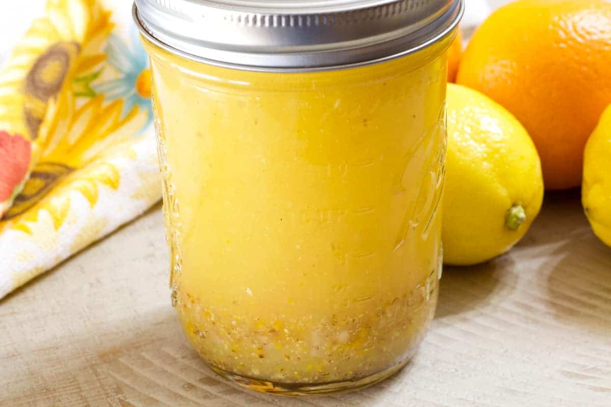 Side view of a jar of salad dressing, an orange, and tow lemons.