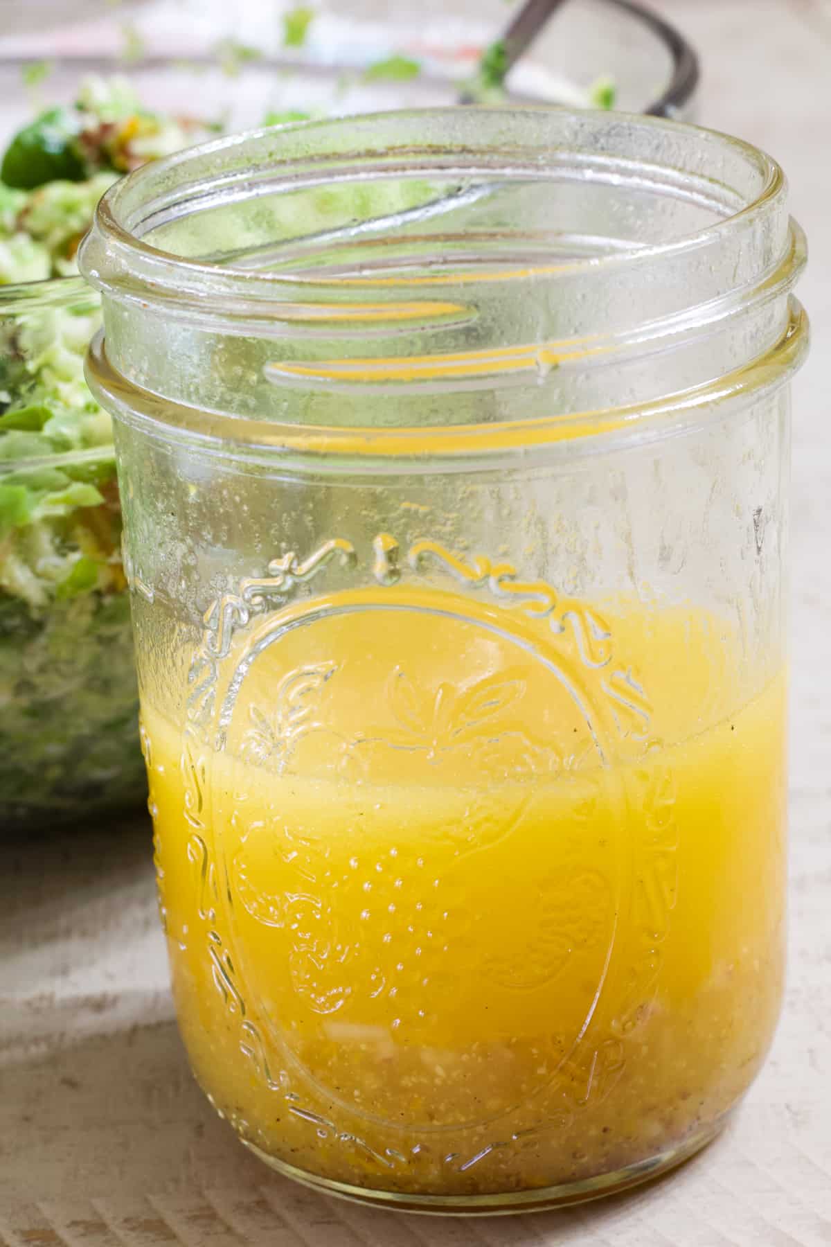 Close up view of a half full jar of citrus vinaigrette in front of a bowl of salad.