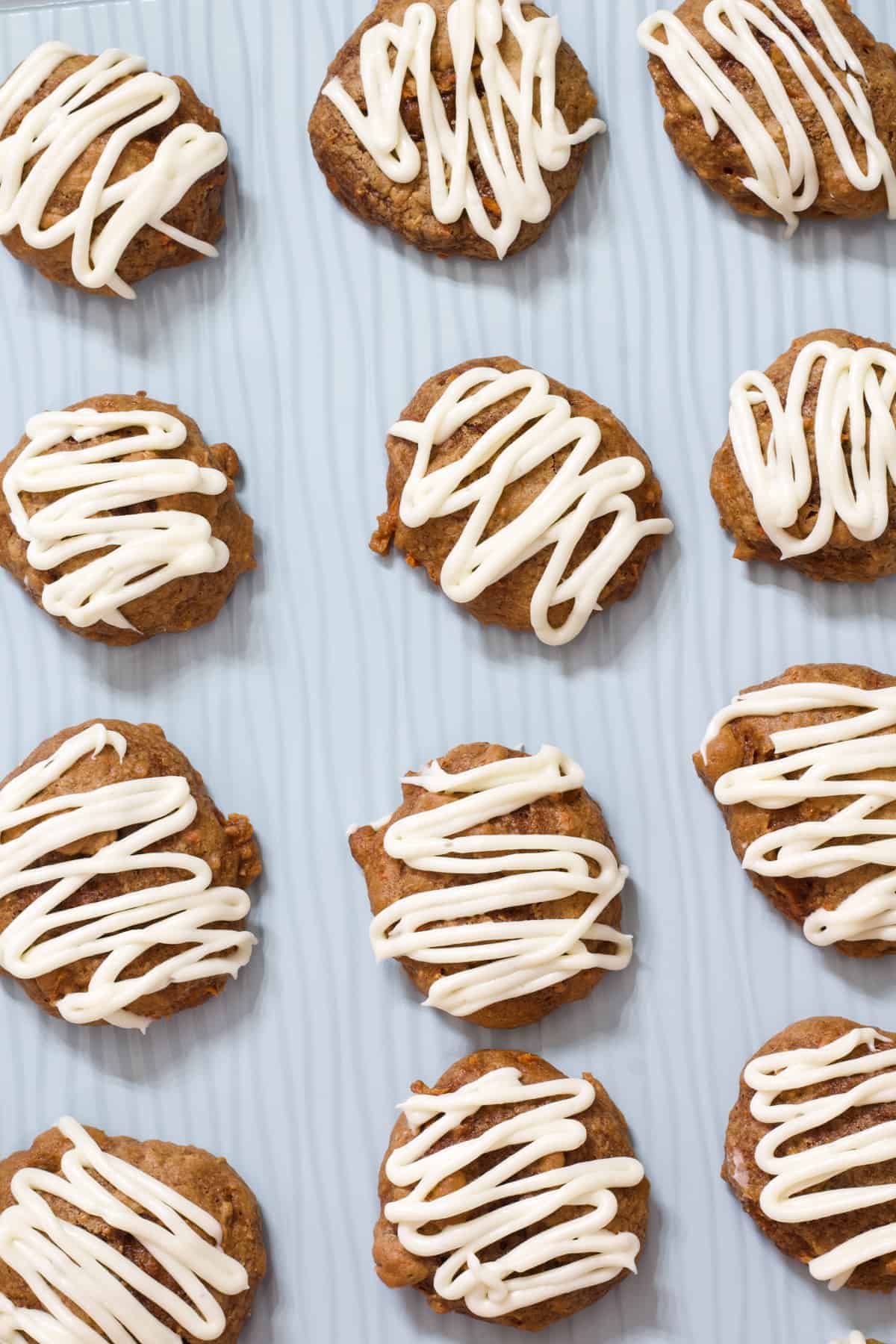 Overhead view of carrot cake cookies on a light blue cookie sheet.