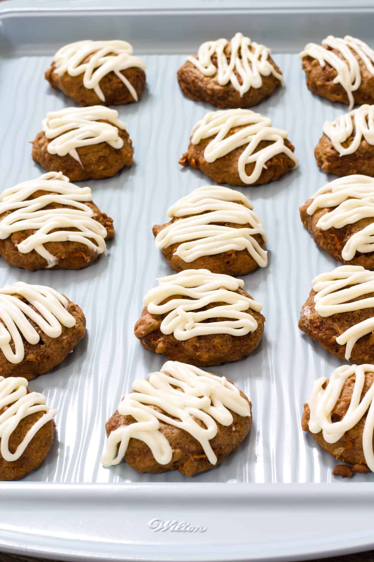 Carrot Cake Mix Cookies frosted with cream cheese frosting on a light blue cookie sheet.