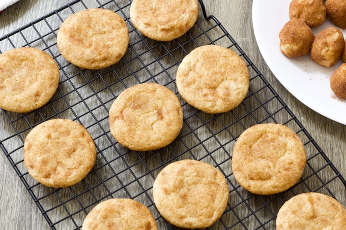 Overhead shot of cookies on a baking rack and the edge of a plate with raw cookie balls on it.