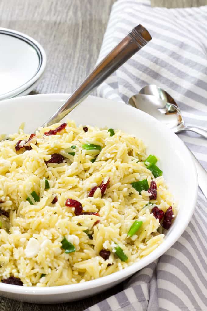 A shallow white bowl with orzo salad with feta and dried cranberries.