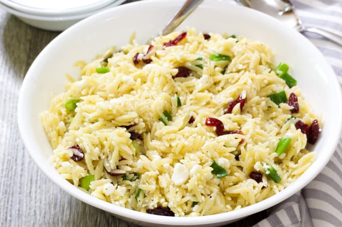 A shallow white bowl with orzo salad with feta and dried cranberries.