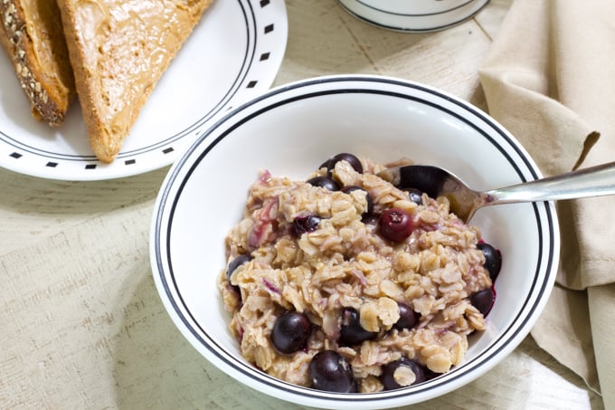 A closer view of a bowl of blueberry oatmeal, cup of coffee and toast.