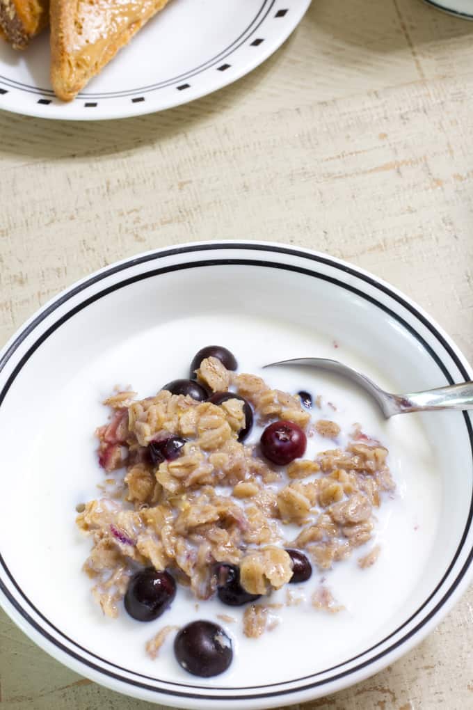 A close up view of a bowl of blueberry oatmeal with milk and a spoon in it.