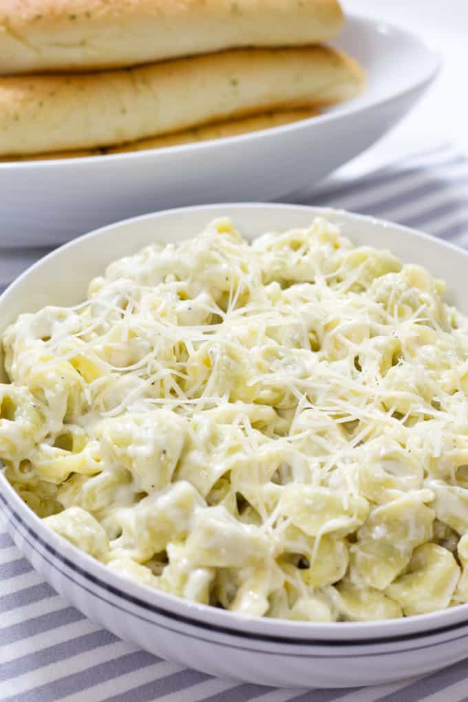 A bowl of tortellini alla panna and you can see part of a bowl of breadsticks. 