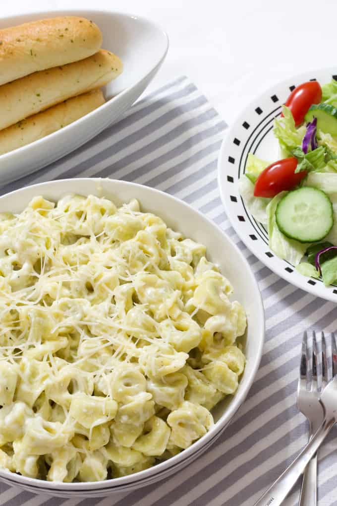 A table with a bowl of pasta, a bowl of breadsticks and a side salad with a fork. 