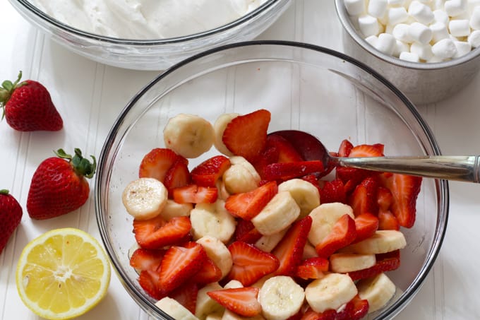 A glass bowl with sliced strawberries and bananas in it.