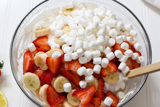 A large glass bowl with cream cheese mixture, fresh fruit and mini marshmallows in it.