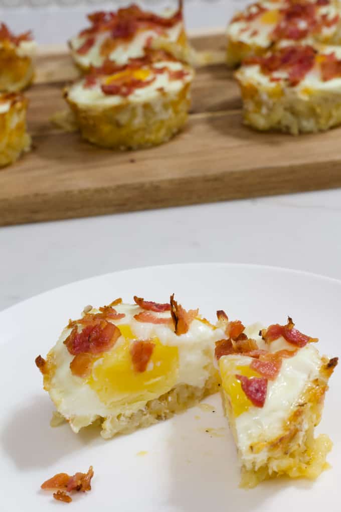 One eggs in a hash brown nest cut in half on a white plate.