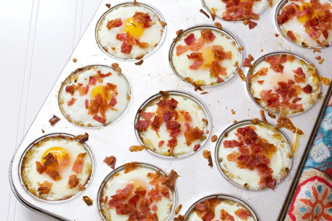 A silver muffin tin filled with a dozen eggs in hash brown nests.