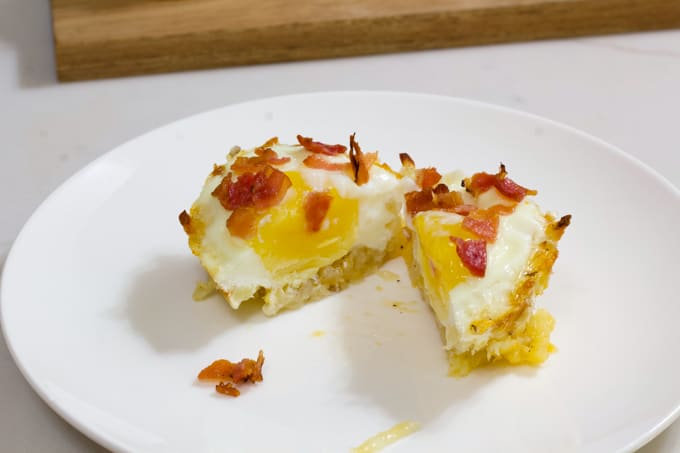 Close up of one eggs in a hash brown nest cut in half on a white plate.