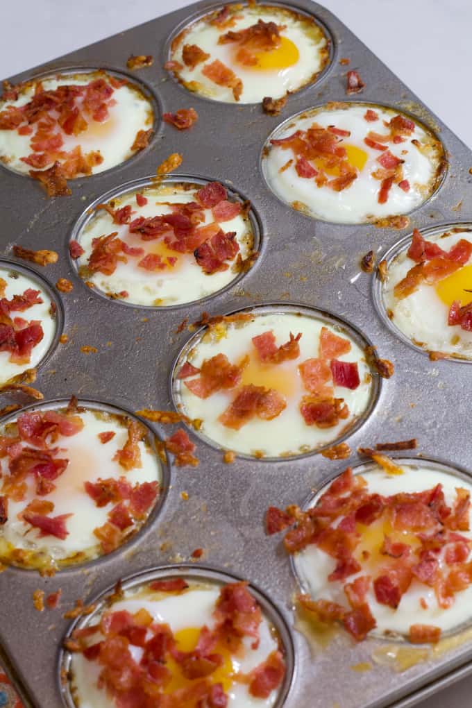 A diagonal angle shot of a silver muffin pan filled with eggs in hash brown nests.