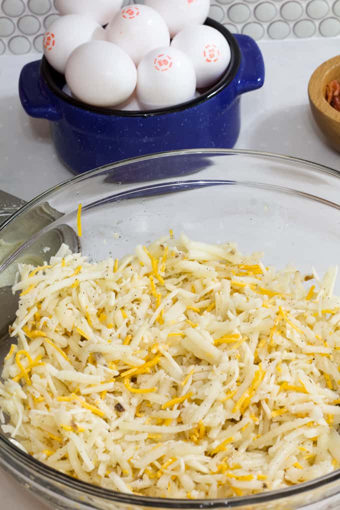 A bowl with hash browns and cheese in the foreground and bowl of eggs in the background.