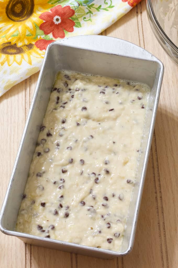 Raw banana bread batter in a silver loaf pan on a wooden background.