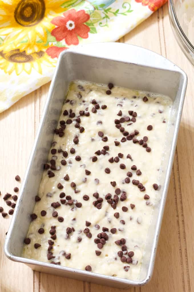 A silver loaf pan with bread batter in it topped with mini chocolate chips.