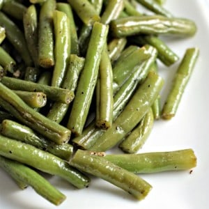 Close up view of a serving of green beans on a whit plate.