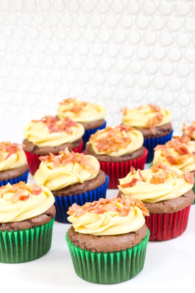 a dozen frosted cupcakes topped with bacon bits sitting on a white countertop.