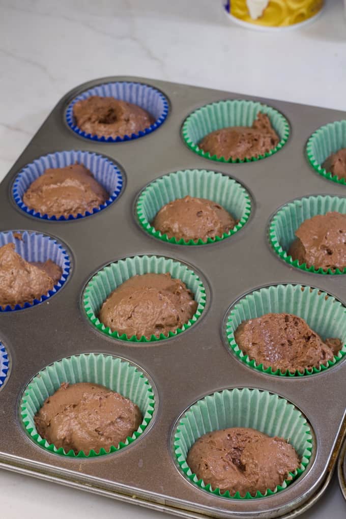 a 12 cup muffin tin filled with paper liners and raw cupcake batter in each cup.