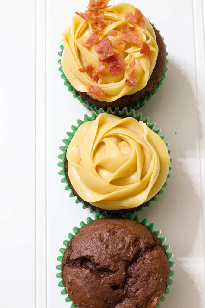 Three chocolate cupcakes, one without frosting, one with frosting and one with frosting and bacon.