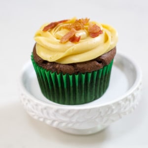 One chocolate cupcake on a white pedestal topped with caramel frosting and bits of bacon.