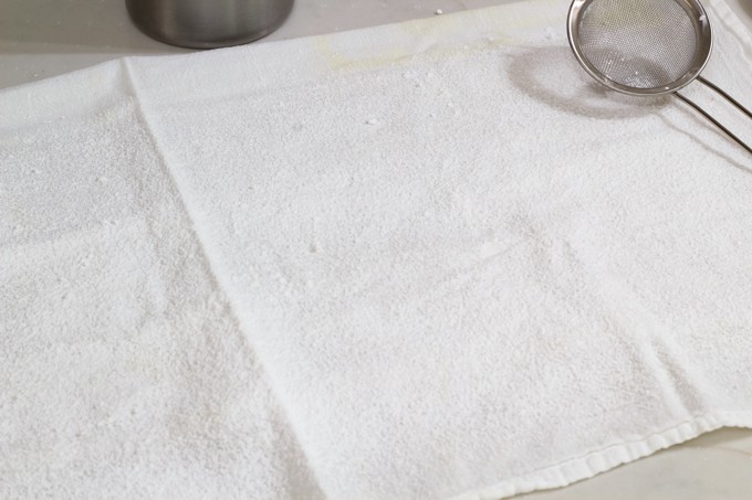 A tea towel sprinkled with powdered sugar with a metal mesh strainer sitting on it.
