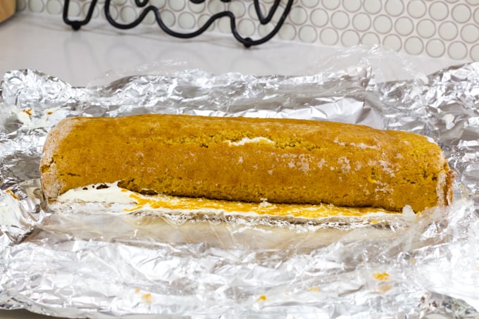 The pumpkin roll laying on the plastic wrap and foil after being refrigerated.