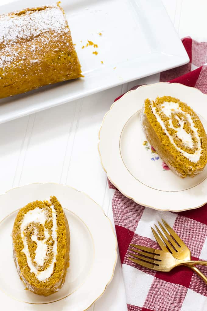 Overhead shot of a pumpkin roll and two pieces on plates with two gold forks sitting nearby.