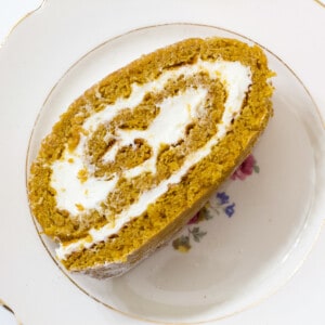 One piece of delicious gluten free pumpkin roll on a white plate with gold trim.